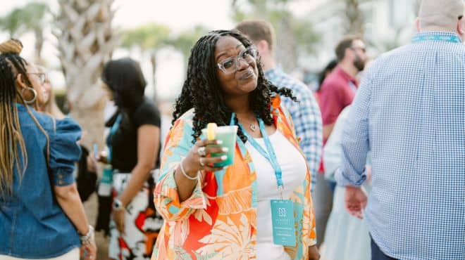 A woman wearing an orange shirt and holding a drink smiling at the camera