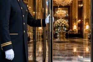A uniformed doorman in white gloves opening the door to a luxury hotel lobby
